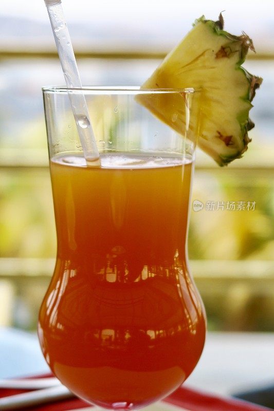 “橙色日落”不含酒精的鸡尾酒/鸡尾酒饮料在节日的飓风杯与菠萝装饰和稻草，印度酒吧背景照片